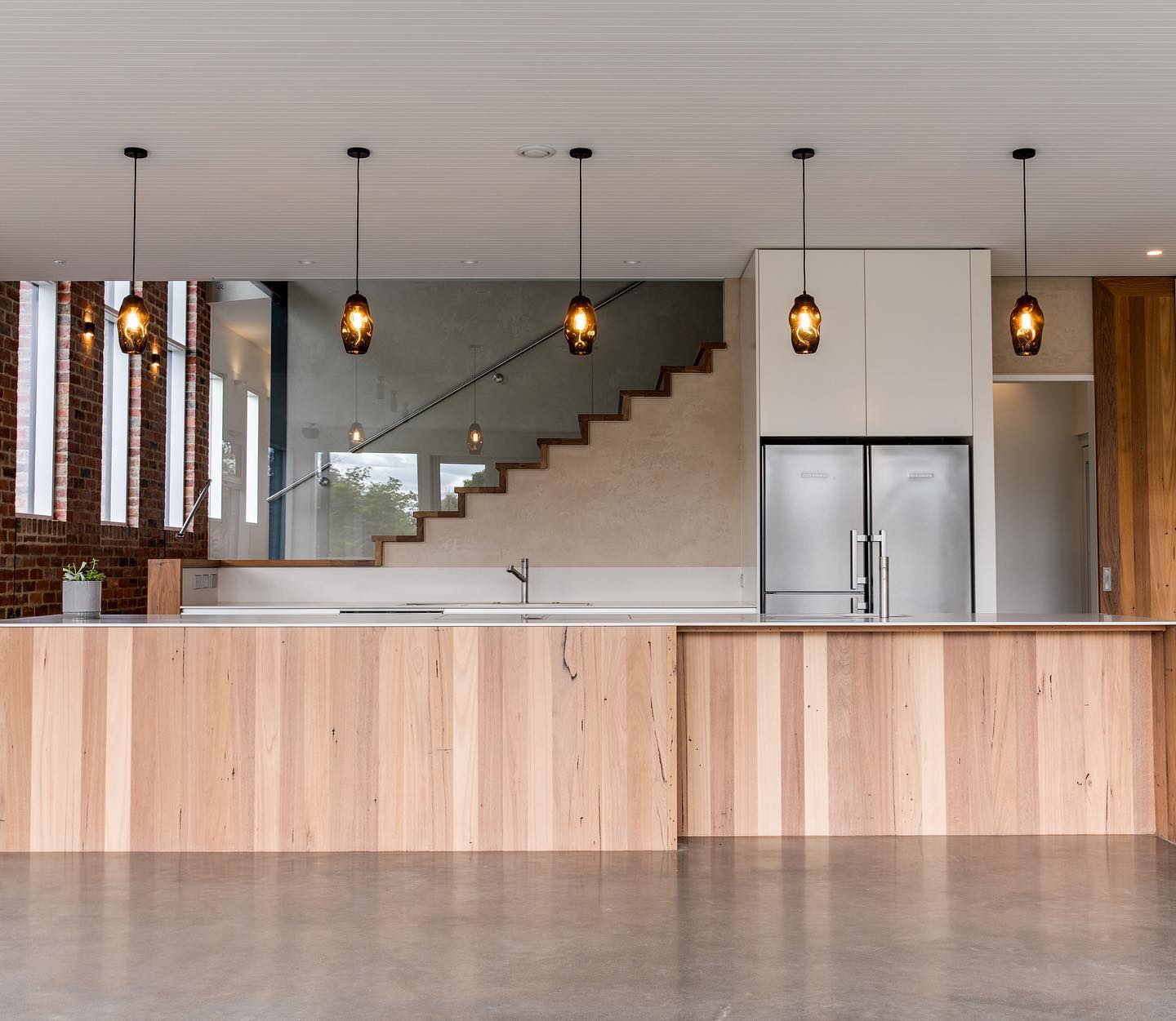 Open-plan kitchen with a timber island bench, pendant lighting and exposed brick