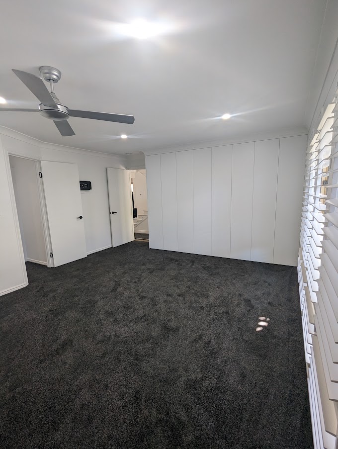Living room with dark carpet, plantation shutters and a ceiling fan