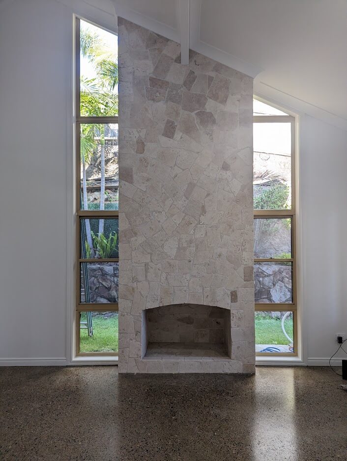 Living space with a stone feature fireplace between full-height windows and polished concrete floors