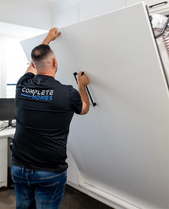 A Complete Homes team member carrying a sheet of plasterboard on site