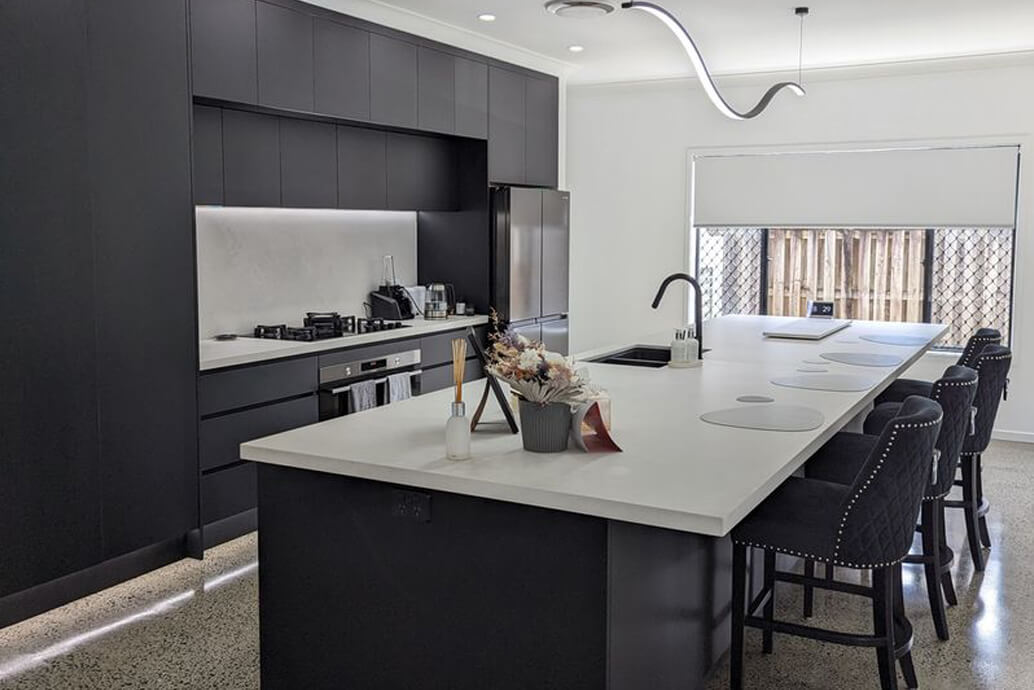 Renovated kitchen with dark cabinetry, a stone island bench and polished concrete floors