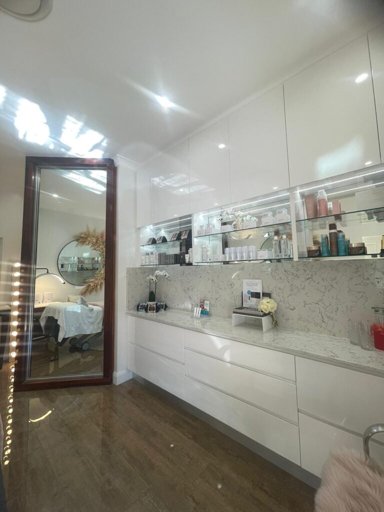 Salon retail wall with gloss white cabinetry and lit product shelving, Varsity Lakes