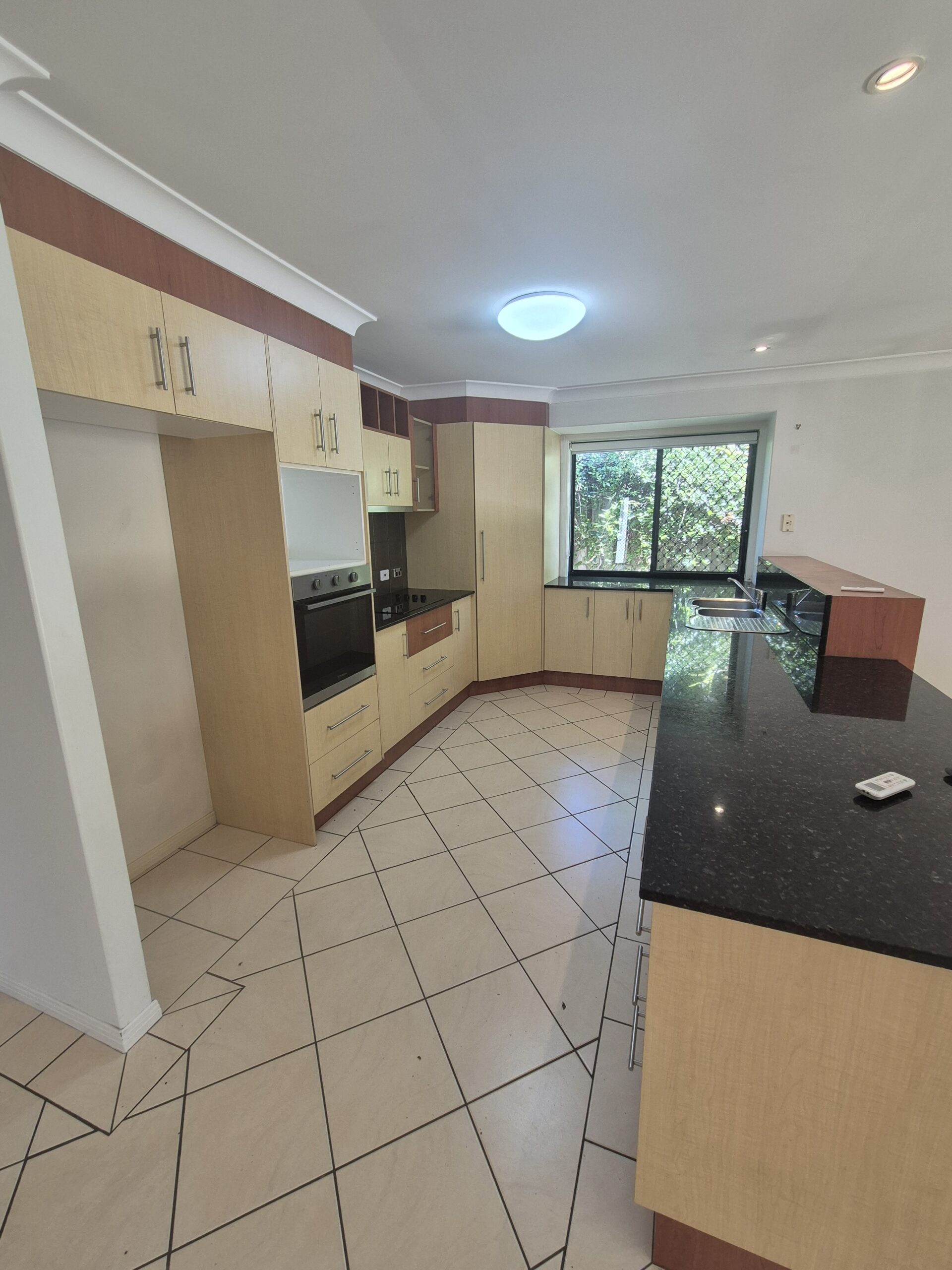 Before renovation: the original kitchen with cream and timber cabinetry and a dark benchtop, Robina