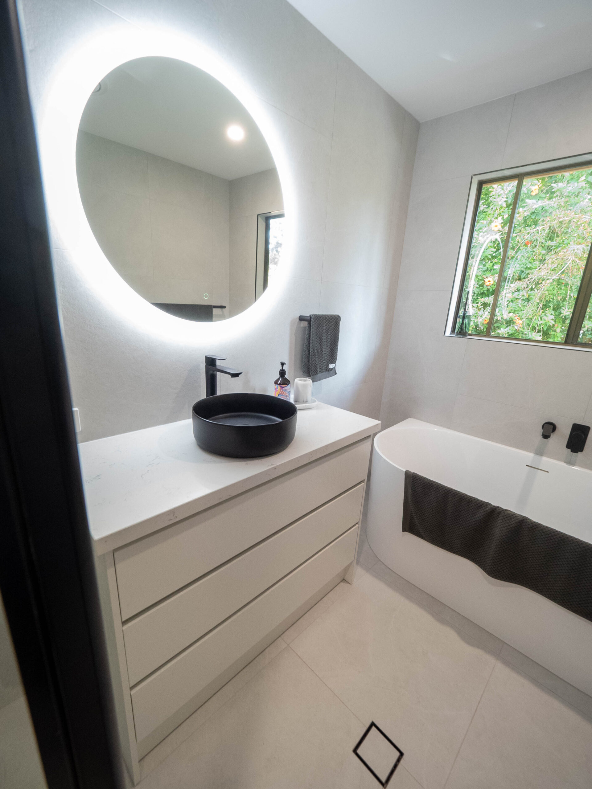 Renovated bathroom vanity with a round backlit mirror, black vessel basin and bath alongside, Lower Beechmont