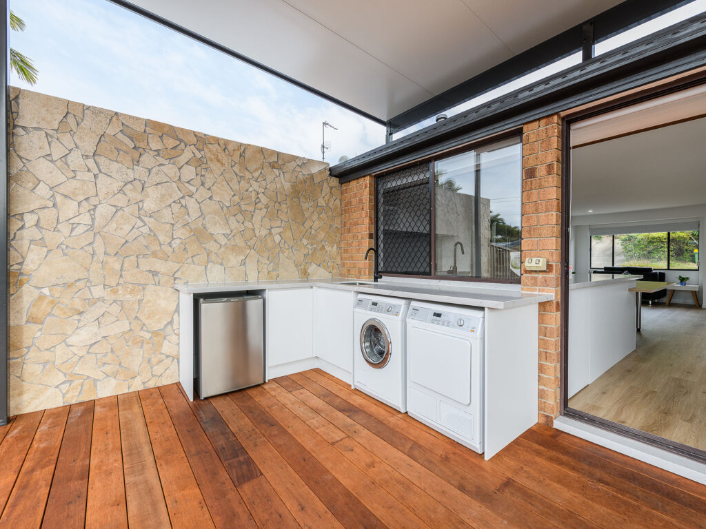 Covered outdoor laundry area with washer and dryer, sandstone feature wall and hardwood decking, Arundel