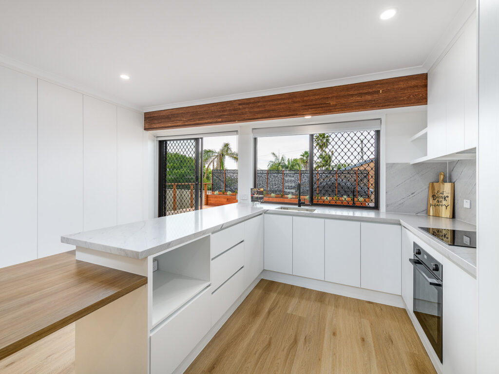 Renovated U-shaped white kitchen with a window above the sink and timber feature beam, Arundel