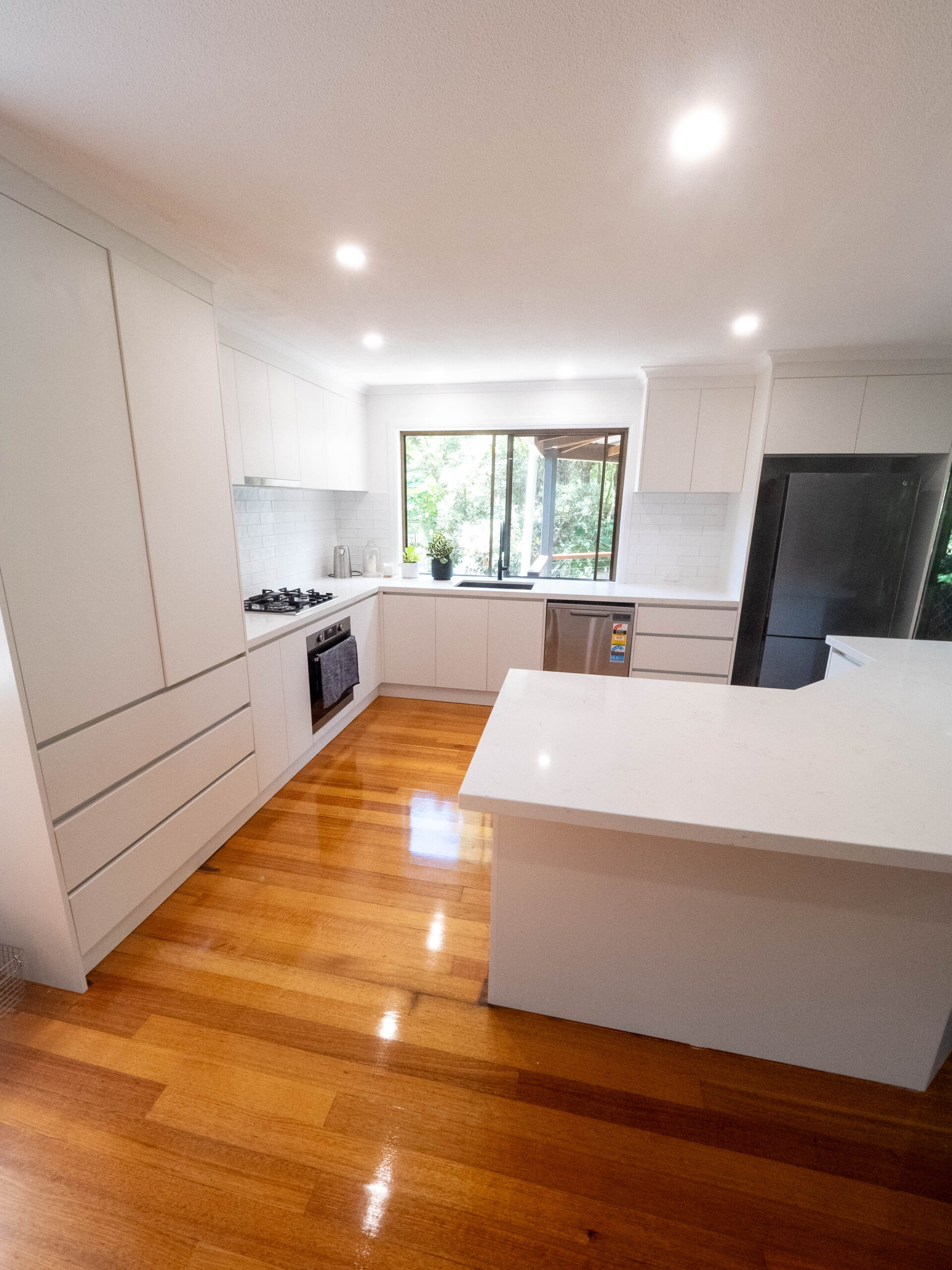 Renovated white kitchen with a stone island bench and polished timber floors, Lower Beechmont