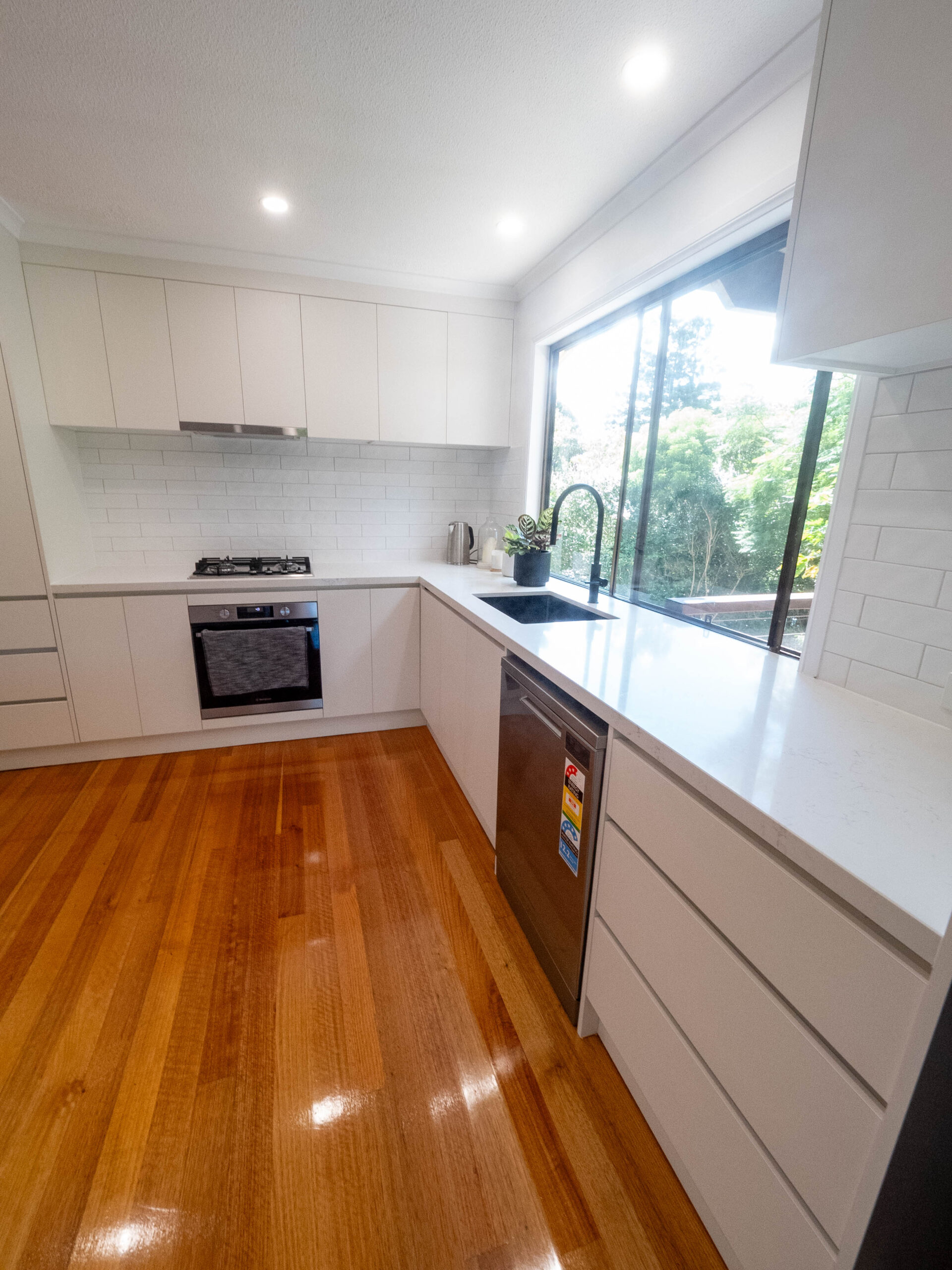 Renovated galley kitchen with white cabinetry, black tapware and polished timber floors, Lower Beechmont