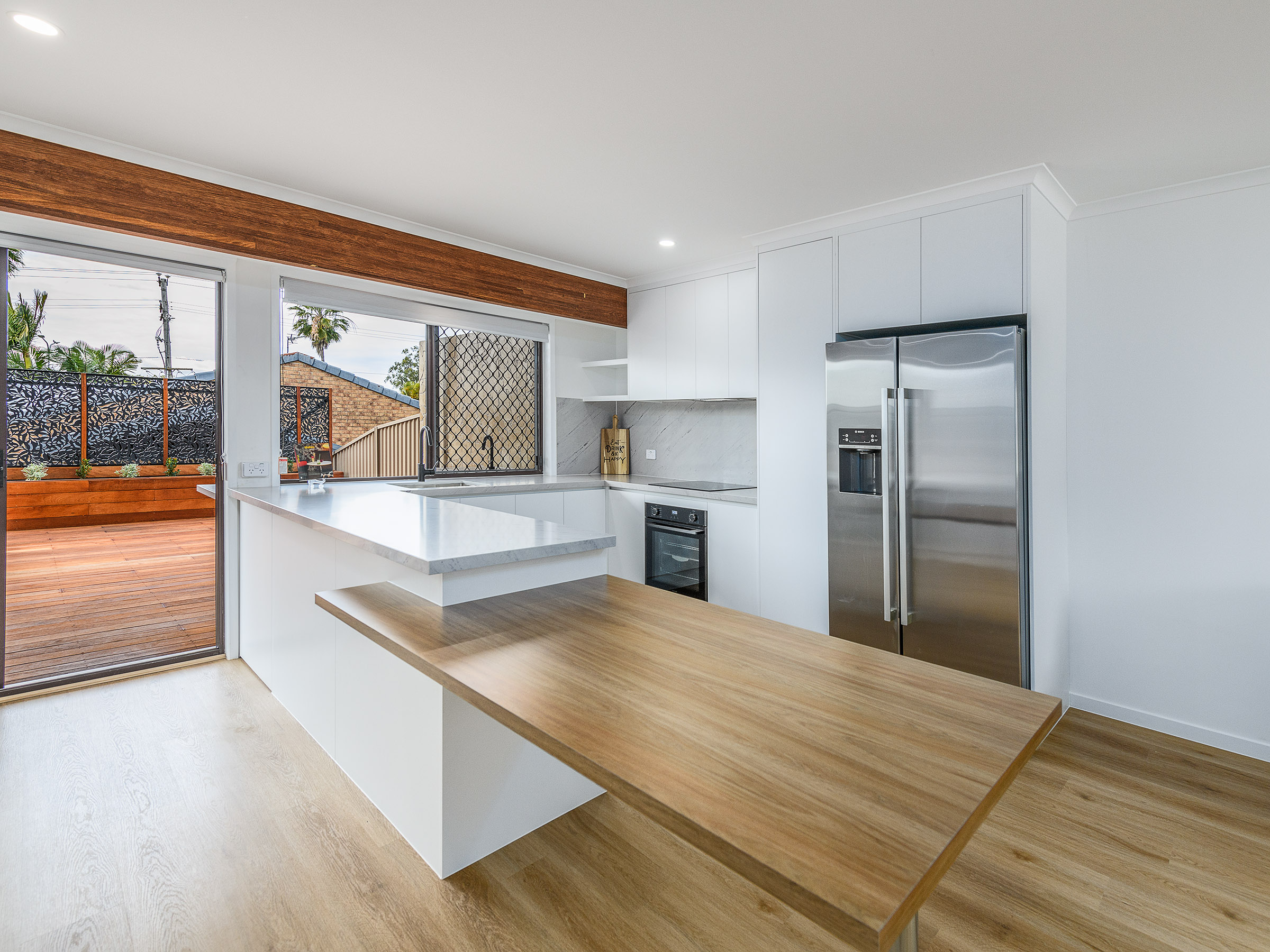 Renovated white kitchen with stone benchtops and a timber breakfast bar opening onto a deck